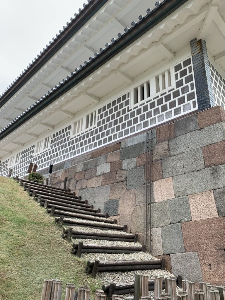 金沢城公園の石垣と白壁の建築。戸室石の色の違いと白い壁、木製の階段が見える