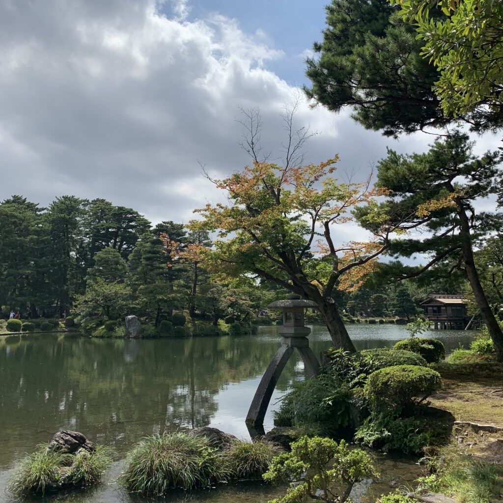 兼六園の霞ヶ池と徽軫灯籠。池の水面を背景に、二本脚の石灯籠と松、庭園の樹木が見える