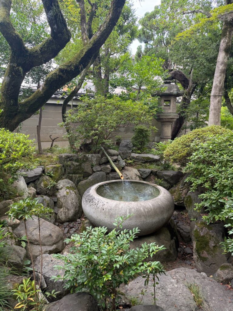 京都の茶席の庭に設えられた石の水鉢と竹の筧、石灯籠