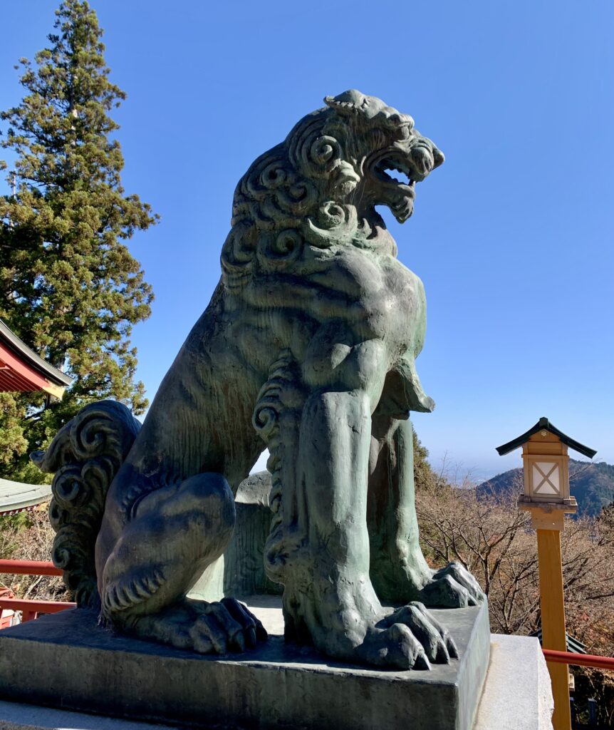 青空を背景に立つ武蔵御嶽神社拝殿前の青銅製狛犬