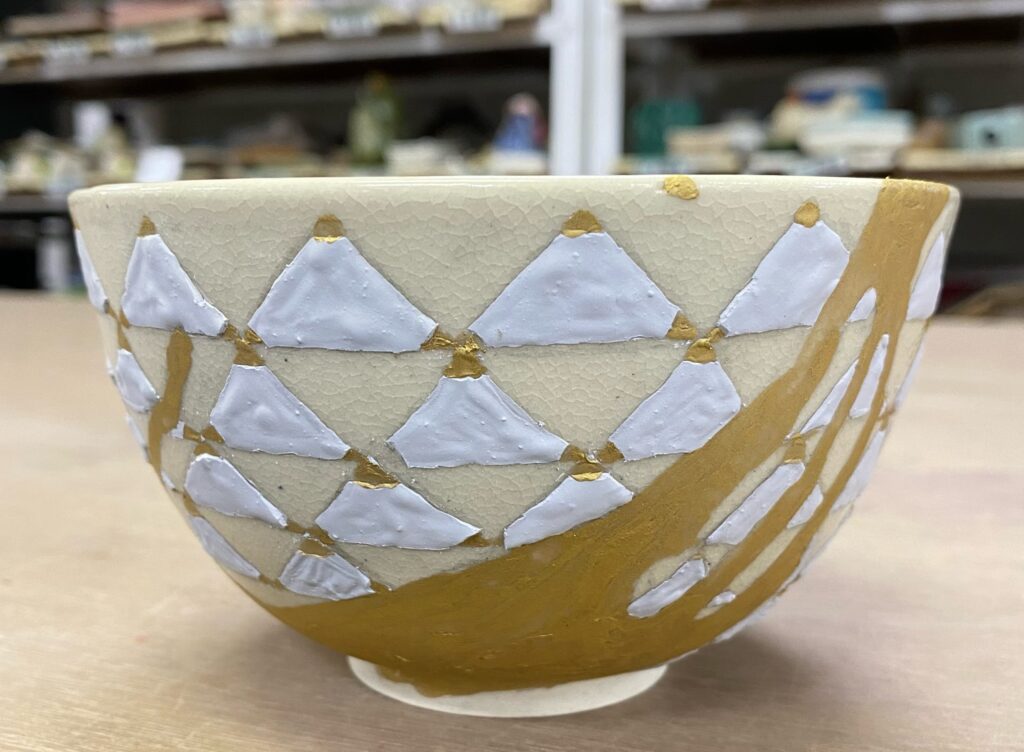 野々村仁清に学んだ色絵茶碗の制作作品。白い三角文様と金彩の大きな曲線が器面を横切る。