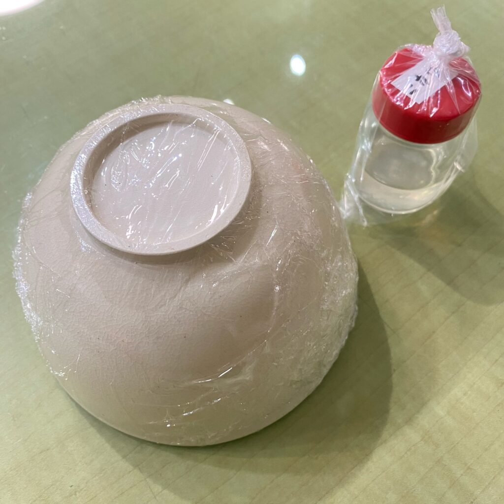 ラップで保護された白い茶碗と上絵付用の液体が置かれた制作風景