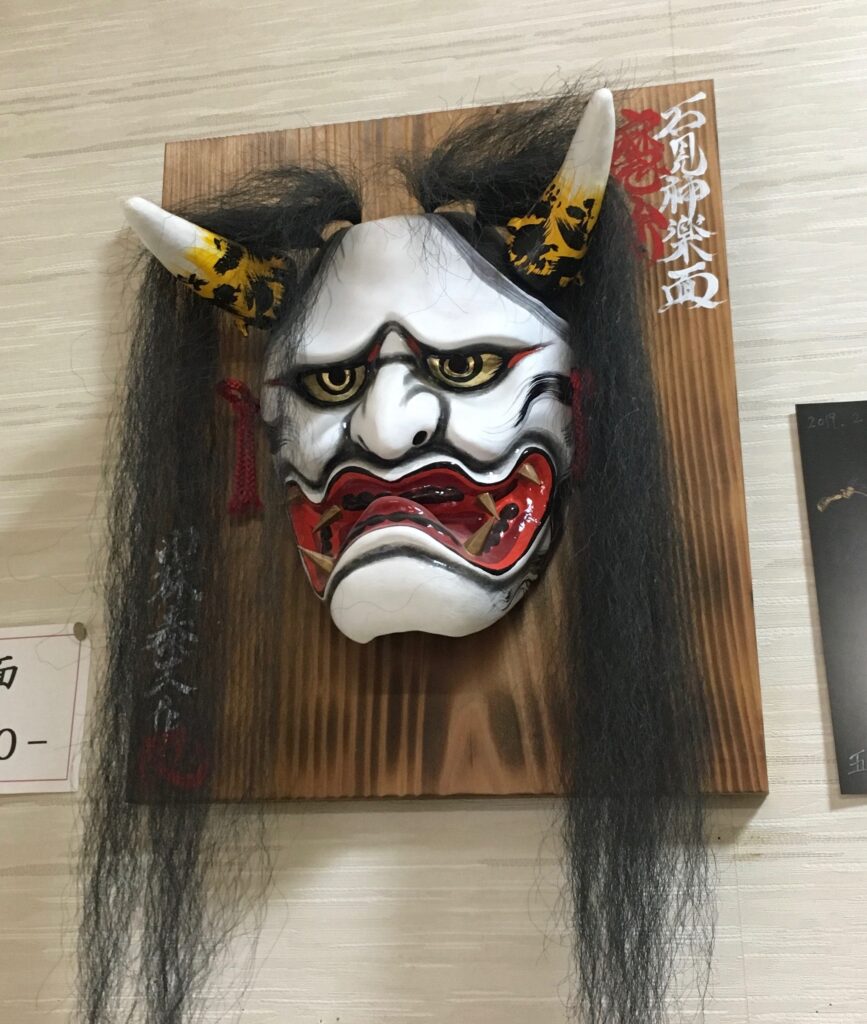 白い顔に赤と黒の彩色、角と黒髪を持つ石見神楽の鬼面