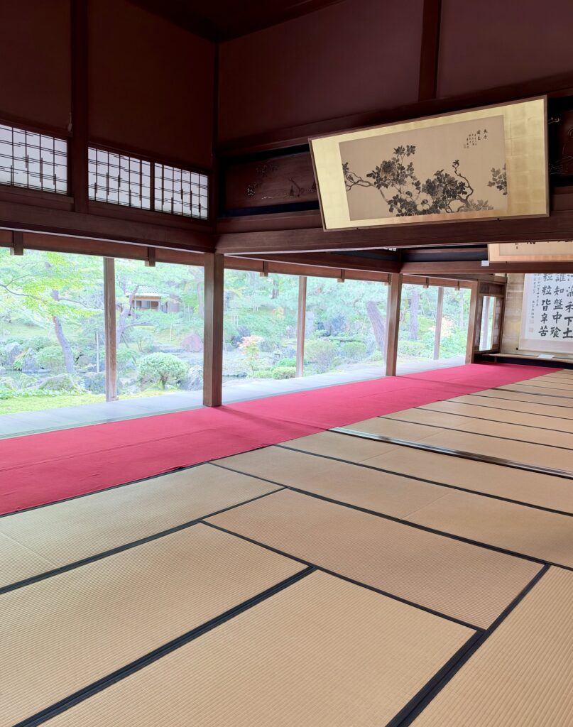 畳敷きの大広間と赤い絨毯、その先に広がる北方文化博物館の日本庭園