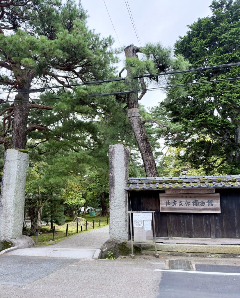 木々に囲まれた北方文化博物館の正門と木造の案内板