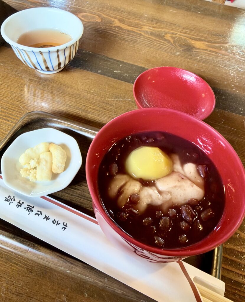 赤い漆器風の器に盛られた栗と餅入りのぜんざい、お茶と漬物