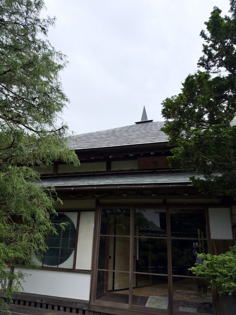 木々に囲まれた三楽亭の正面と特徴的な屋根、丸窓