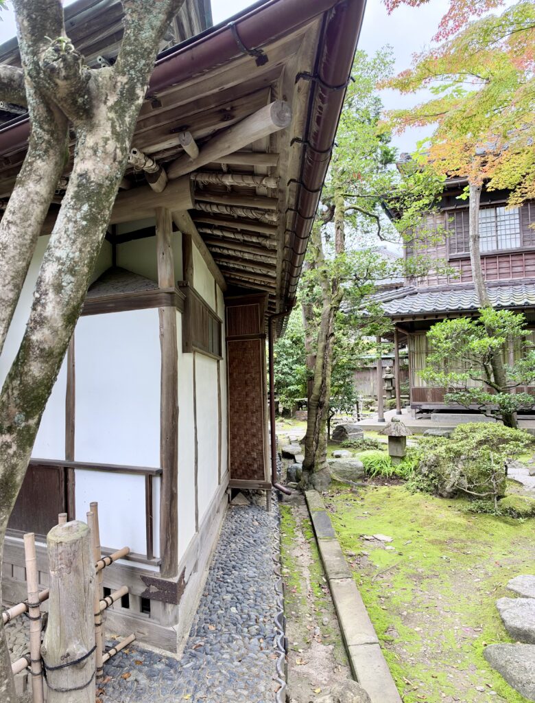 三楽亭の深い軒と木造の柱、奥に伊藤邸が見える庭園風景